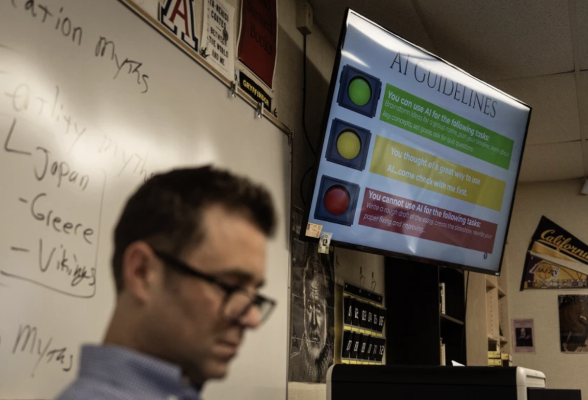 English teacher Casey Cuny reads in his classroom as a screen displays guidelines for using artificial intelligence